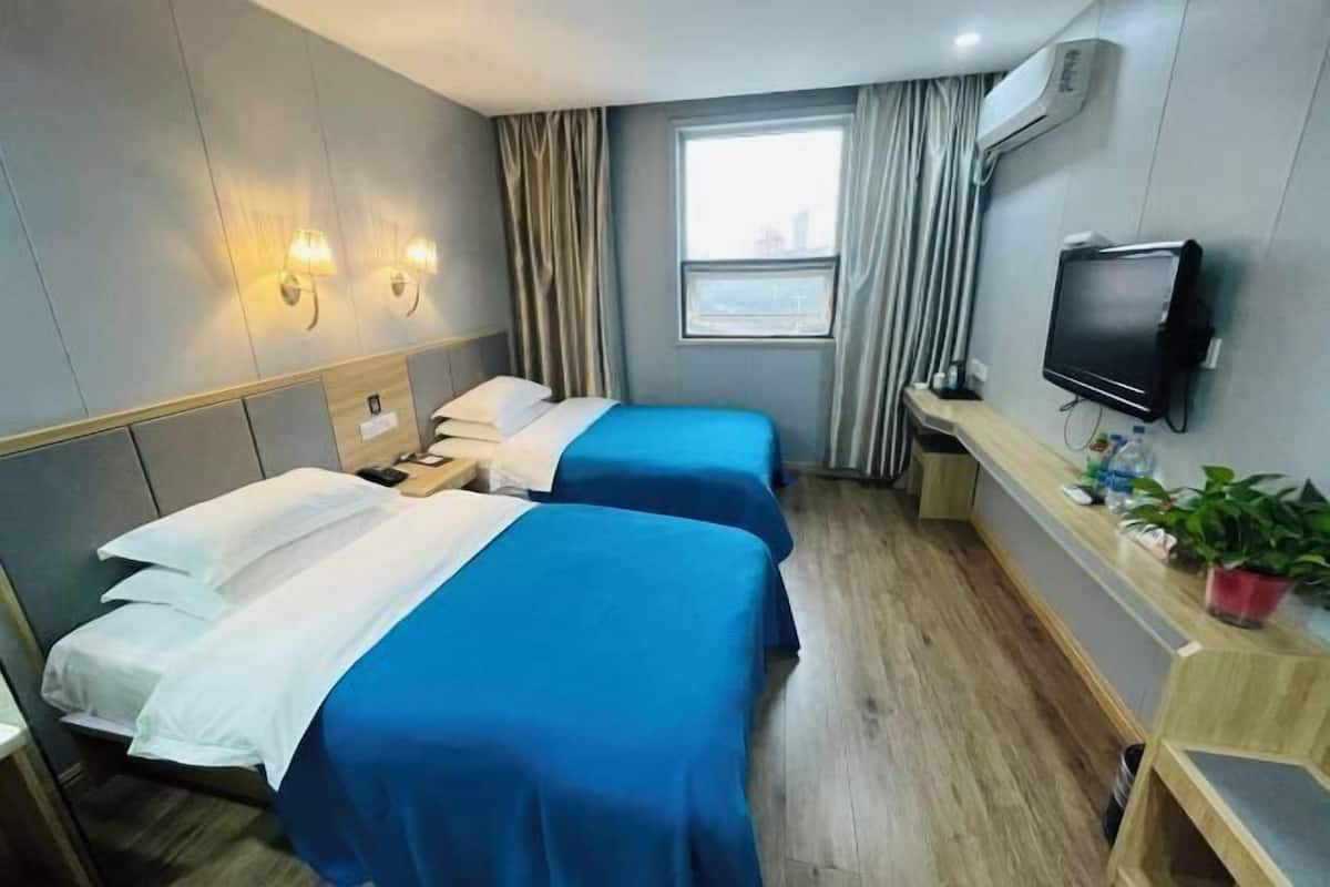 A hotel room with two beds, a TV, a desk with a plant, and a window with curtains.