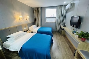 A hotel room with two beds, a TV, a desk, and a window.