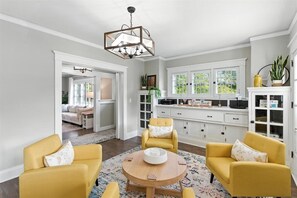 A spacious living room with a round wooden coffee table, two yellow armchairs, and a white sofa. There is a kitchen area with white cabinets and a large window. - Perfect for Weddings, Holidays & Family Gatherings! Pet-Friendly! Sleeps 11 (Dayton)