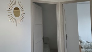 A room with a white wall, a sun-shaped mirror, and a hanging light fixture. - Tastefully renovated apartment close to sea, town and amenities! (Toulon)