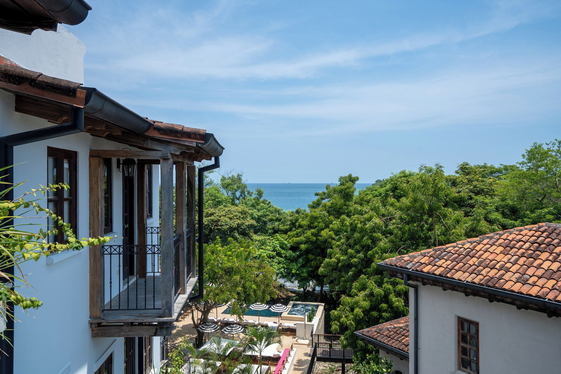 A building with a balcony overlooking a pool area and the sea.