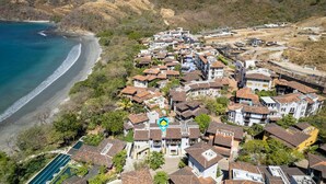 An aerial view of a coastal residential area with houses, a beach, and hills in the background. - Trendy Condo with Modern Decor, Stunning Ocean Views, and Exclusive Beach Club Access (Las Catalinas)