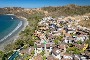 Vista aérea de una zona residencial costera con casas, una playa y colinas al fondo.