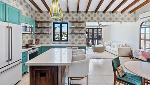 A modern kitchen with teal cabinets, a central island, and a hanging light fixture. - Trendy Condo with Modern Decor, Stunning Ocean Views, and Exclusive Beach Club Access (Las Catalinas)