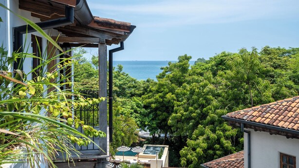 A balcony with a view of the sea, surrounded by lush greenery. - Trendy Condo with Modern Decor, Stunning Ocean Views, and Exclusive Beach Club Access (Las Catalinas)