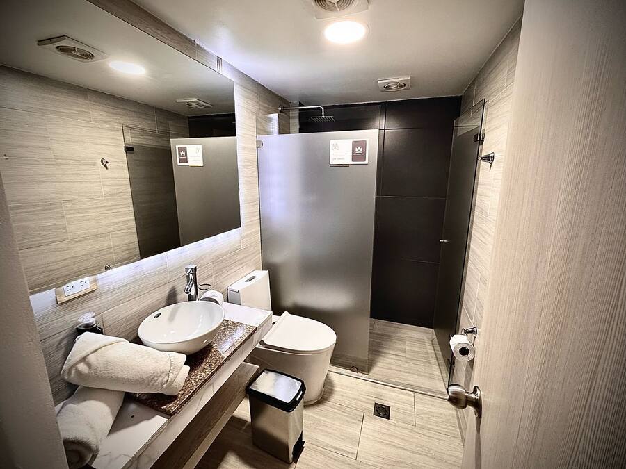 Un baño moderno con un espejo grande, dos lavamanos, un inodoro y una cabina de ducha.