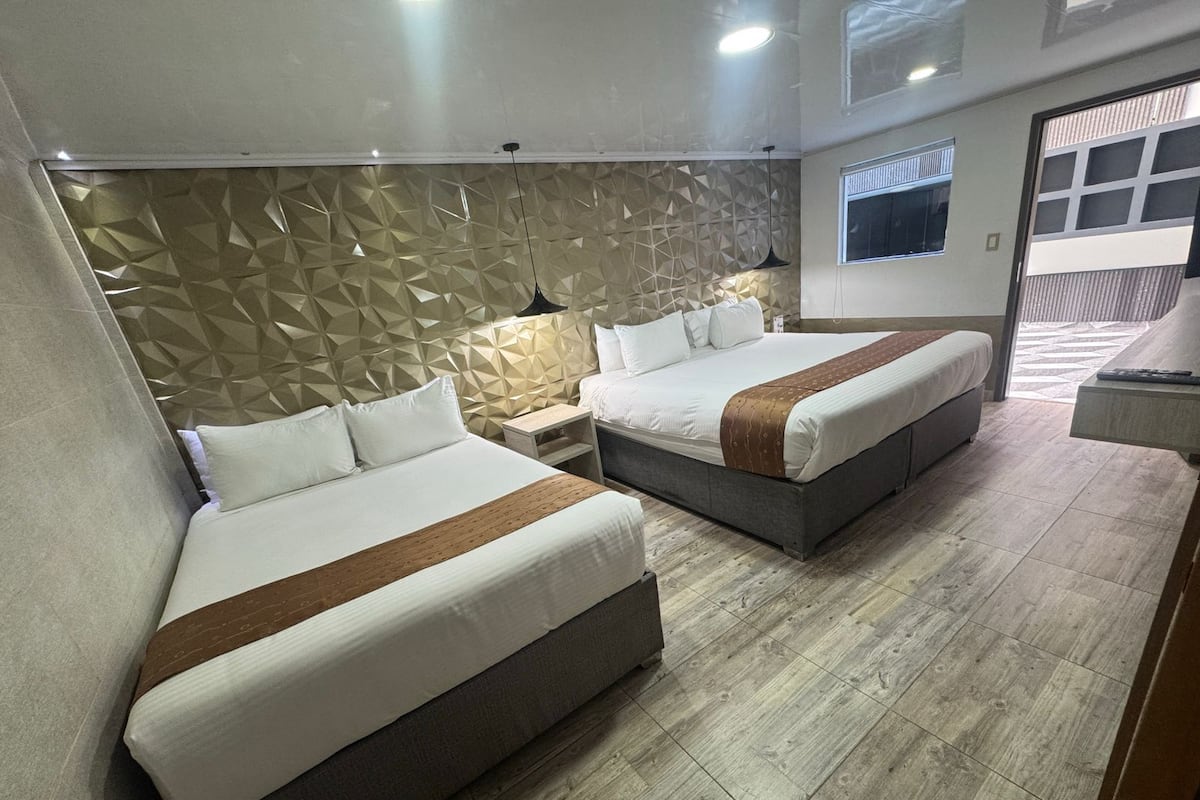Una habitación de hotel con dos camas, un muro con diseño geométrico, suelo de madera y una ventana.