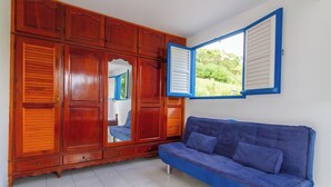 A room with a wooden wardrobe, a blue sofa, and a window with shutters.