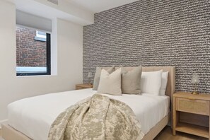 A bedroom with a bed, a patterned headboard, a nightstand, and a window with a view of a brick wall. - Condo for 4 Overlooking Downtown Collingwood (Collingwood)