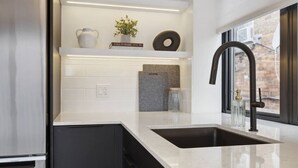 A modern kitchen with a black sink, white countertops, and a window with a view of a brick building.