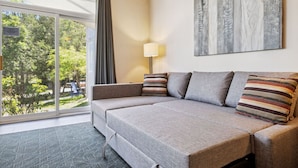 A hotel room with a sofa bed, a lamp, and a view of trees through a large window. - Ground-Floor Cachet Crossing, Steps to BM Village! (The Blue Mountains)