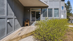 A modern building with a wooden deck, a chair, and a small bush. - Ground-Floor Cachet Crossing, Steps to BM Village! (The Blue Mountains)