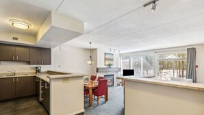 A modern kitchen with a dining area, a fireplace, and a large window with blinds. - Ground-Floor Cachet Crossing, Steps to BM Village! (The Blue Mountains)