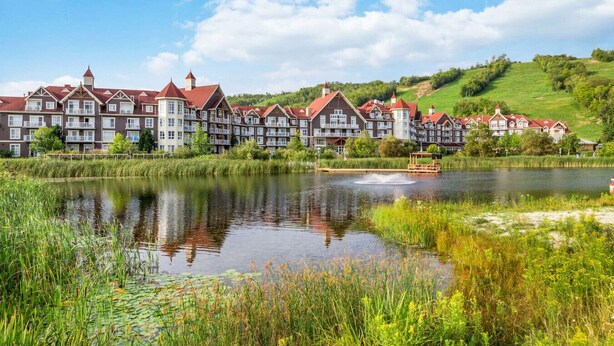 A hotel with multiple buildings, a pond, and a grassy hill in the background. - Ground-Floor Cachet Crossing, Steps to BM Village! (The Blue Mountains)