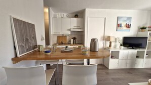 A modern kitchen with white cabinets, a wooden countertop, and a dining area with white chairs. - Royan - A TRULY CHARMING GEM for this APARTMENT with a soothing ambiance - WIFI (ROYAN)