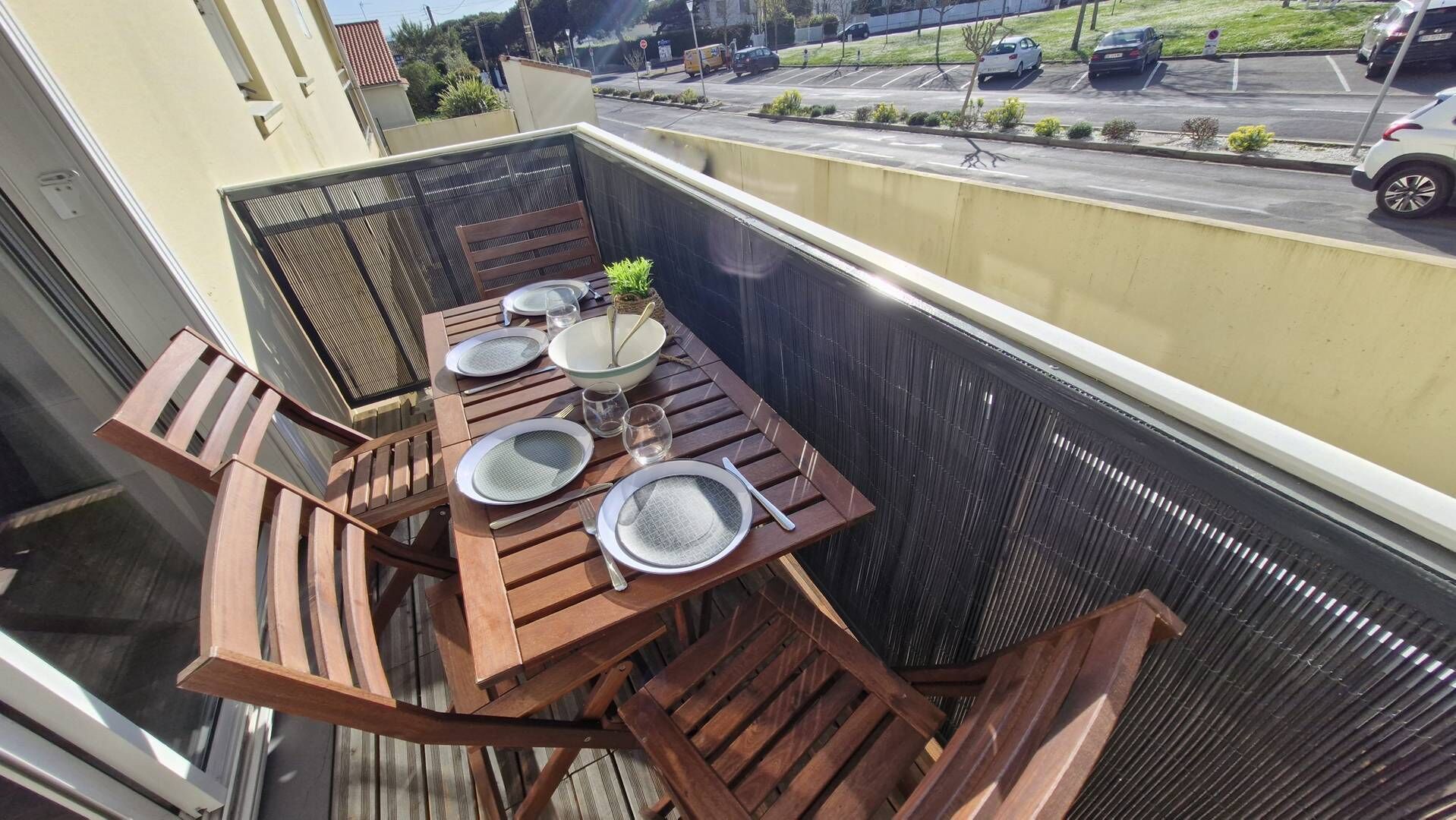 Een balkon met een houten tafel voor twee personen, compleet met borden, glazen en bestek.