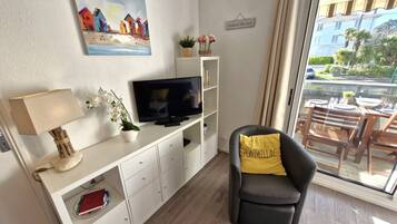 A modern living room with a flat-screen TV, a sofa with a yellow pillow, a small table with a bowl and glasses, and a painting on the wall.