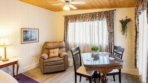 Una habitación acogedora con techo de madera, un sofá de cuero marrón, una mesa de comedor de vidrio con sillas, una lámpara pequeña y un cuadro en la pared.