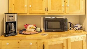 Una kitchenette con armarios de madera, una cafetera, un microondas, un tazón de bocadillos y un hervidor de agua.