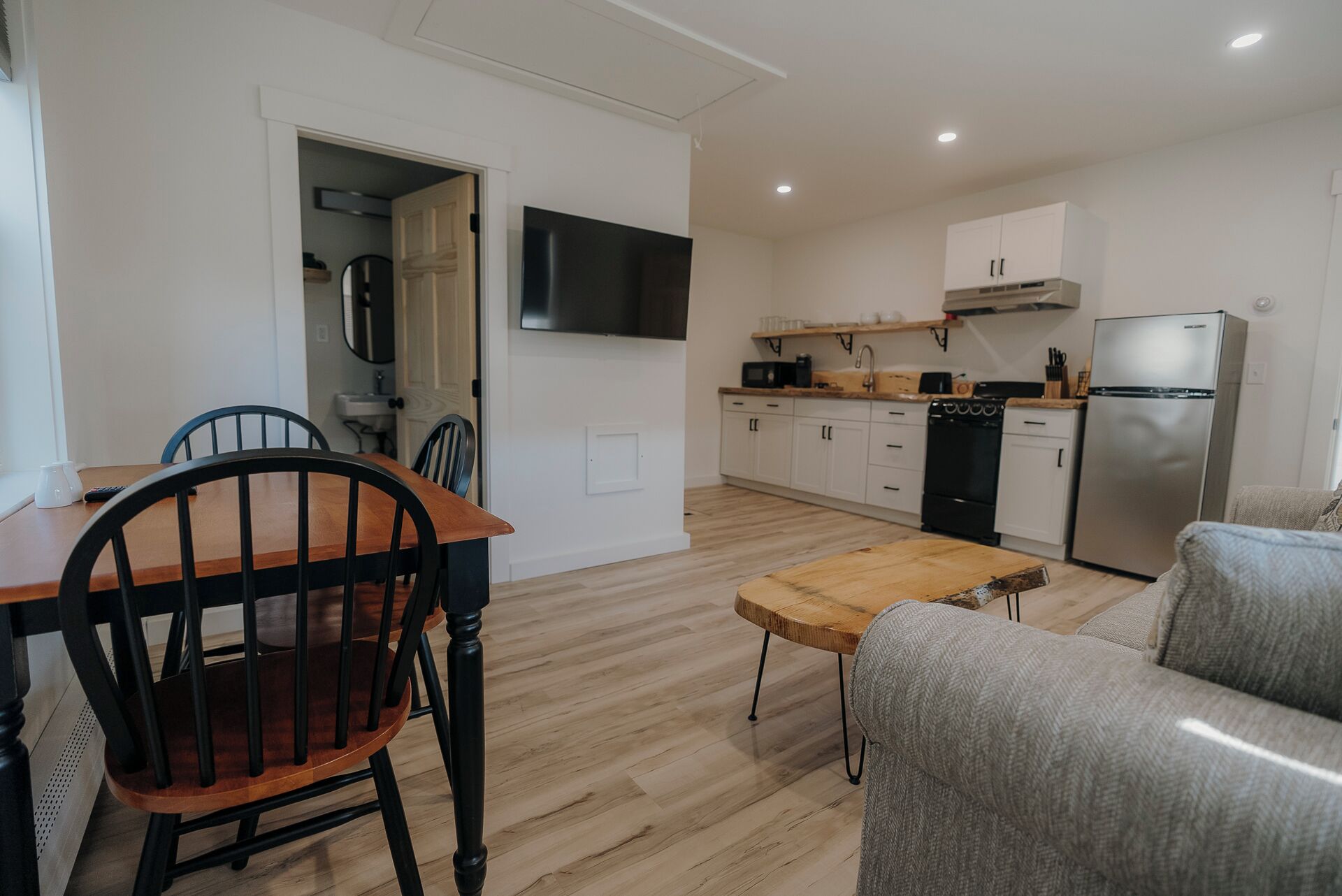 A compact kitchen with a dining area, a TV mounted above the counter, and a refrigerator.
