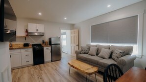 A modern kitchen with white cabinets, a black stove, and a stainless steel refrigerator. There is a wooden dining table with chairs and a grey sofa with patterned cushions. - Bingham Motor Inn (Bingham)