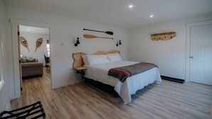 A bedroom with a wooden bed, a wooden headboard, a wooden floor, a white door, and a wooden shelf with hooks.