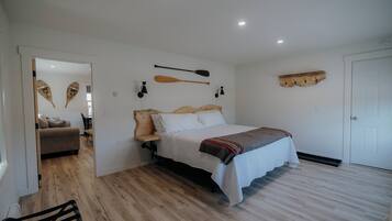 A bedroom with a wooden bed, a wooden headboard, a wooden floor, a white door, and a wooden shelf with hooks.