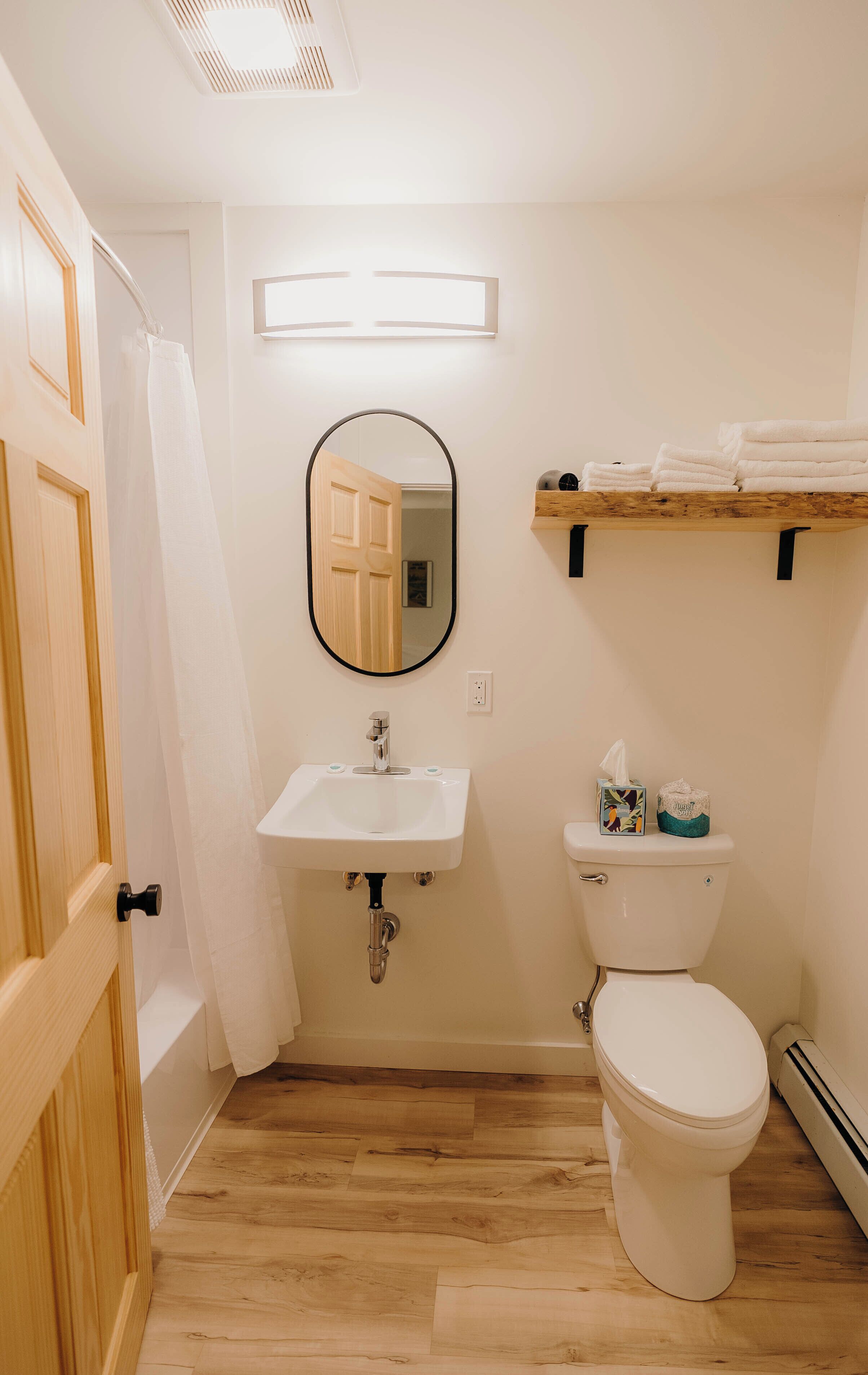 A bathroom with a wooden door, white sink, mirror, toilet, and a shelf with towels.