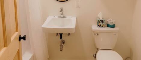 A bathroom with a wooden door, white sink, mirror, toilet, and a shelf with towels.