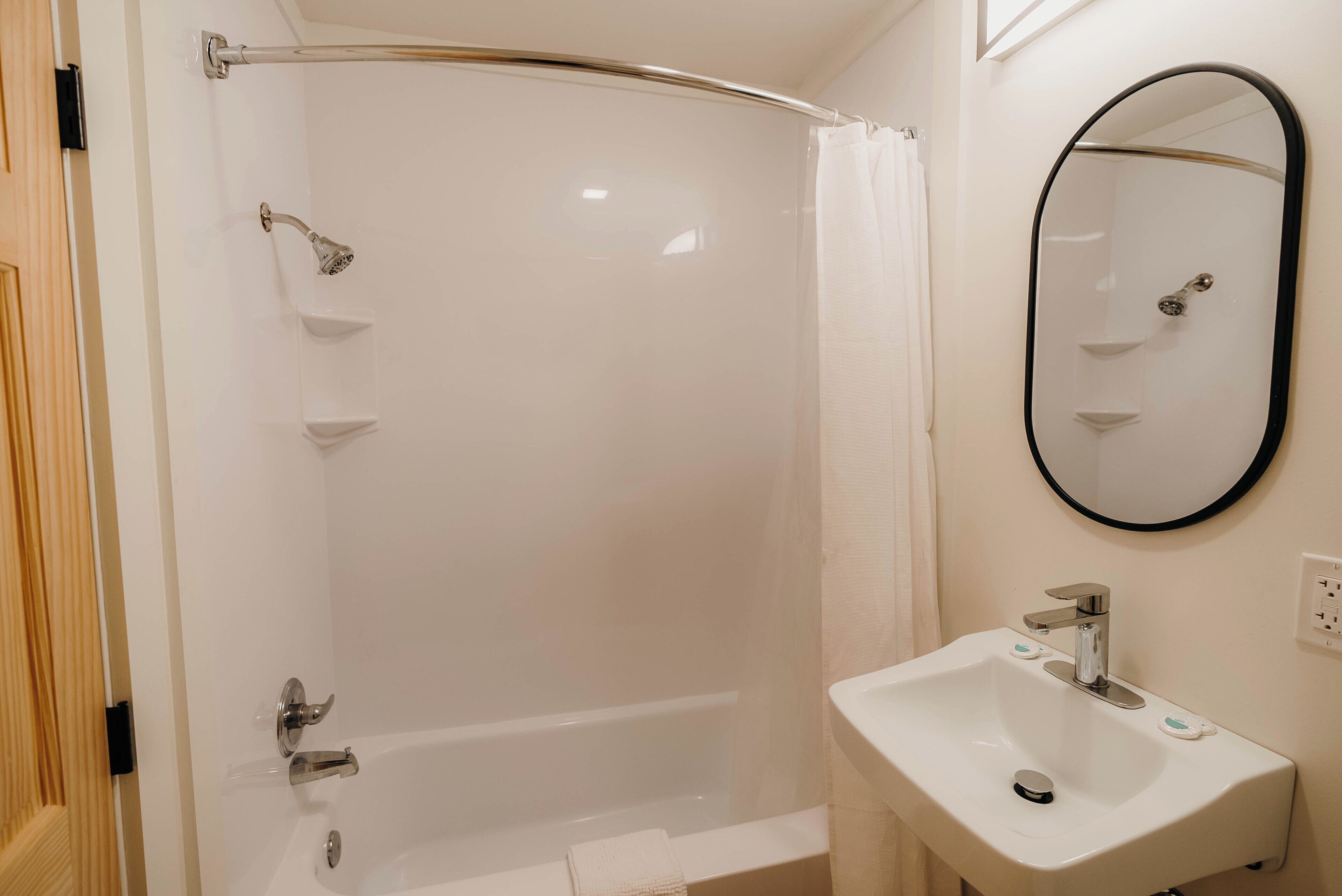 A bathroom with a glass-enclosed shower, a white sink, and a mirror with a black frame.