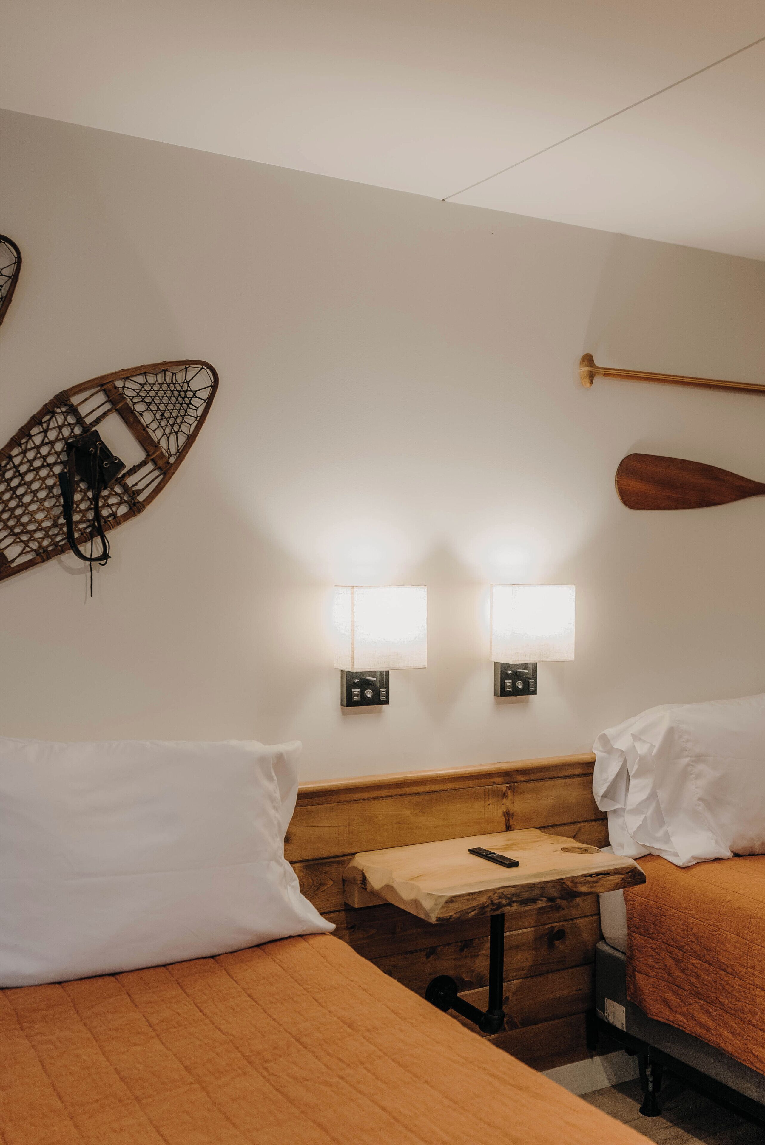 A hotel room with two beds, wooden headboards, a small wooden table, and wall-mounted lights.
