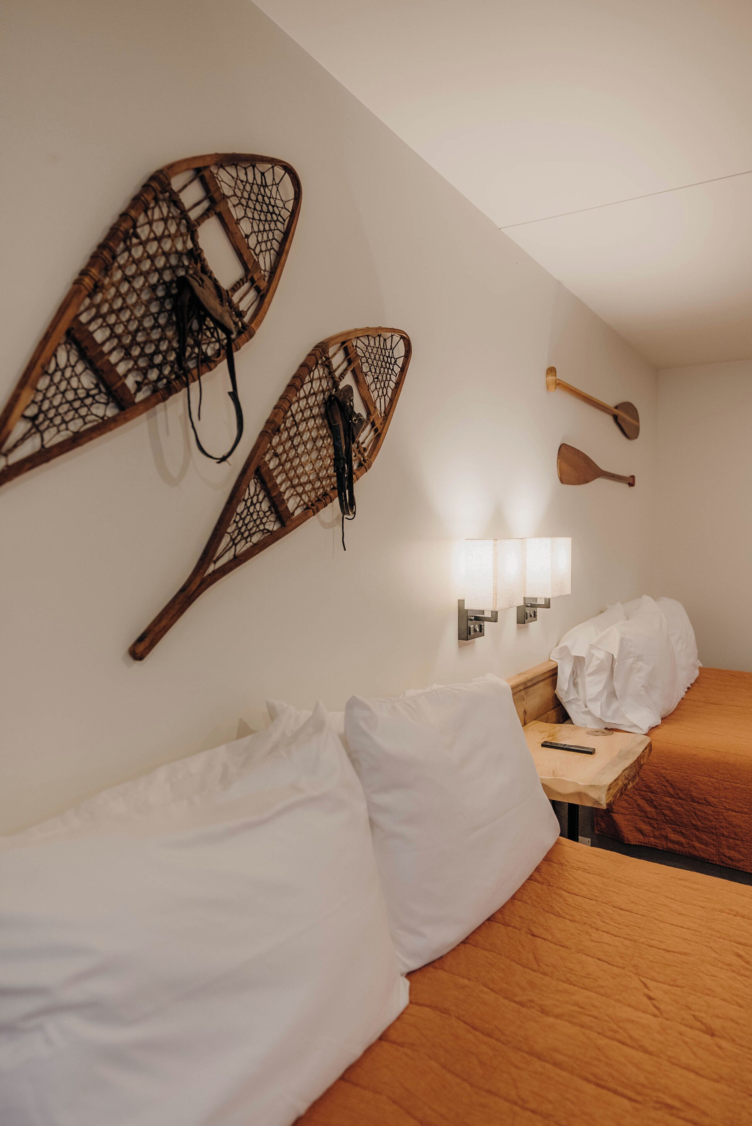 A hotel room with two beds, a wooden headboard, a wall-mounted light fixture, and two paddleboards.