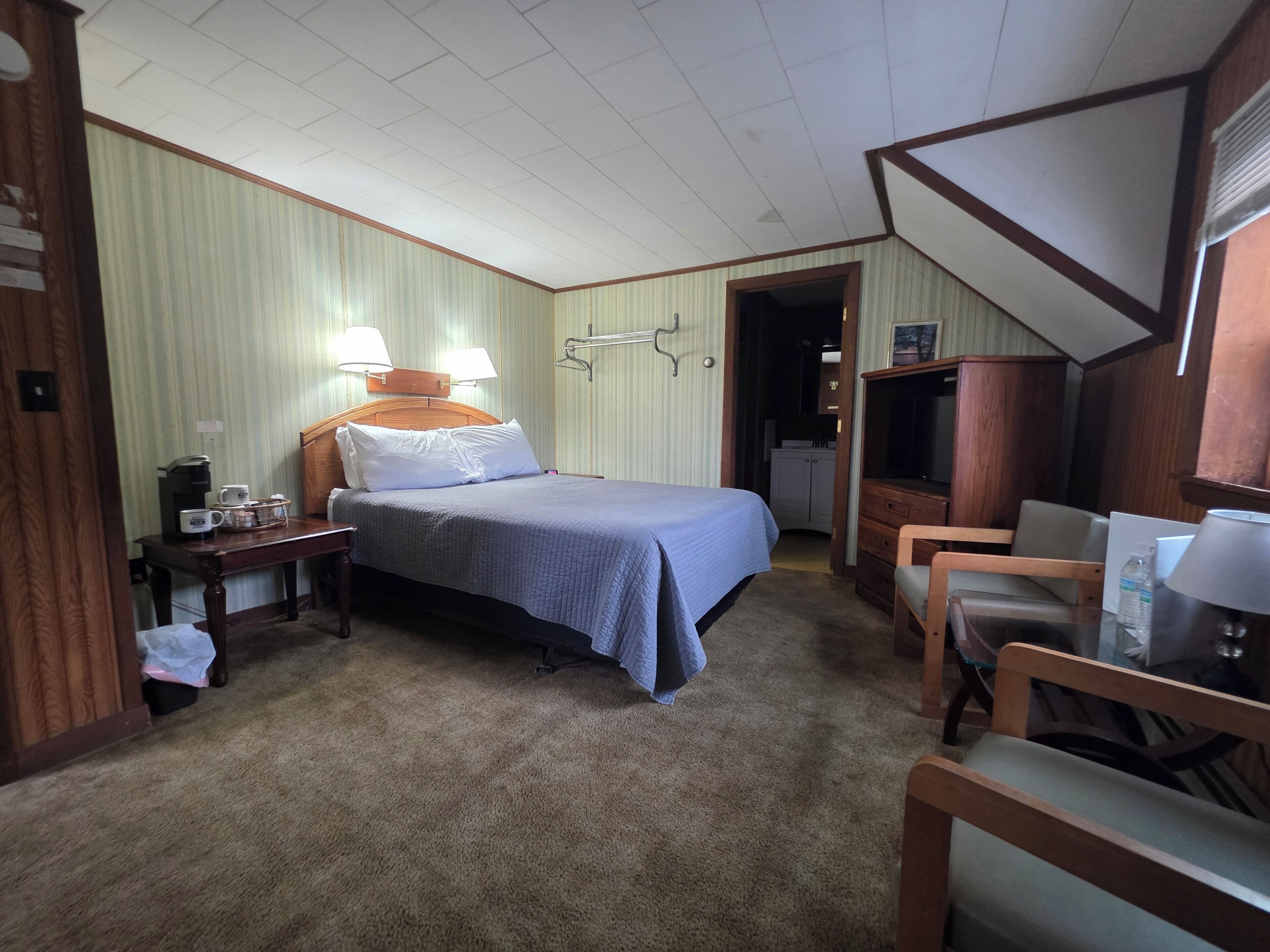 A hotel room with a bed, bedside table, lamp, and a desk with a chair.