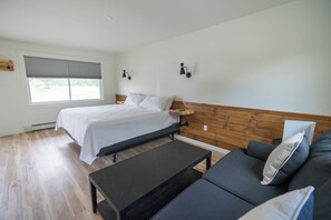A bedroom with a bed, a wooden headboard, a dark-colored table, and a gray sofa.