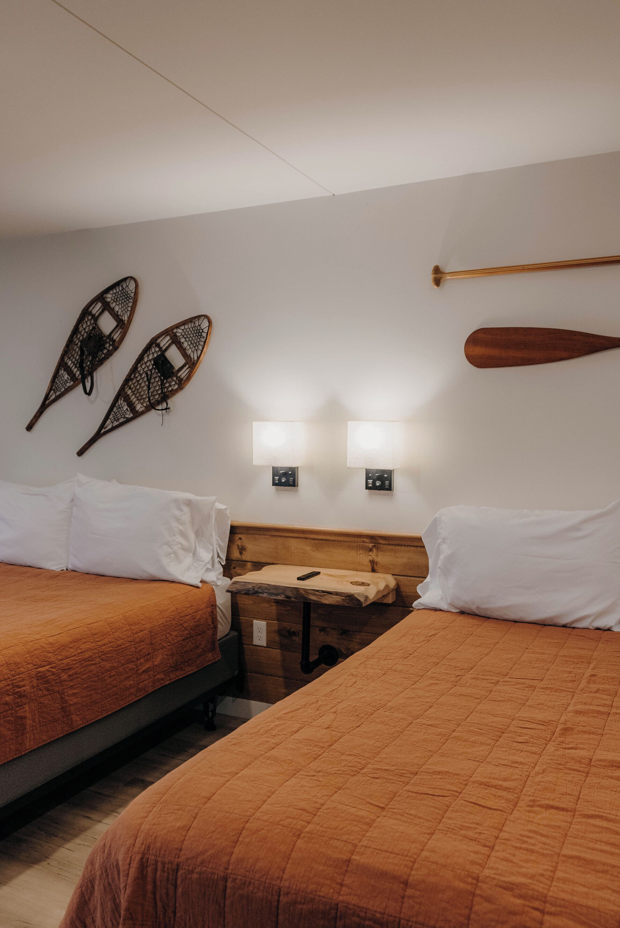 A hotel room with two beds, a wooden headboard, wall-mounted lights, and decorative wooden paddles.