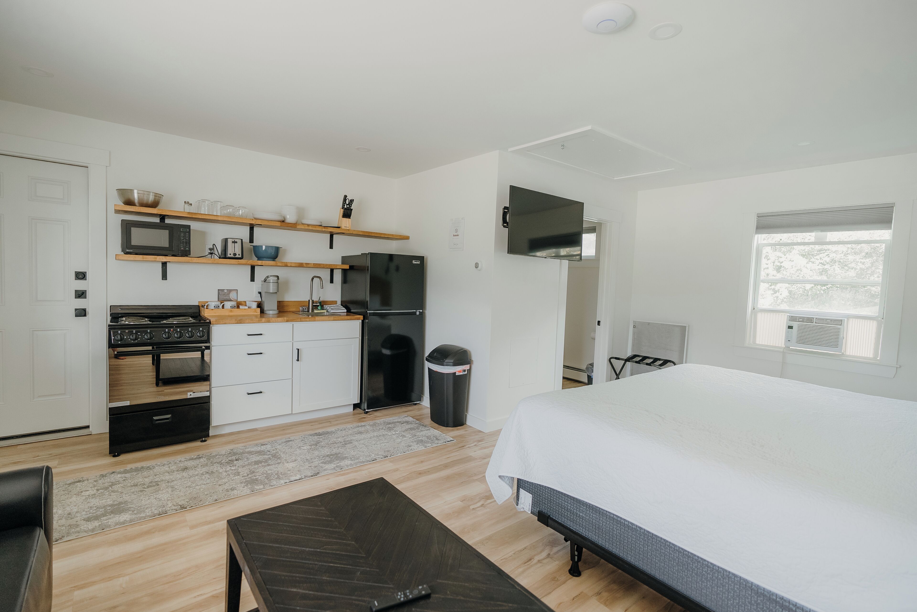 A compact hotel room with a kitchenette, a bed, a small table, and a window.