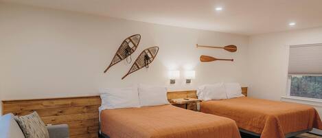 A hotel room with two beds, a sofa, a small table, and a window with blinds.