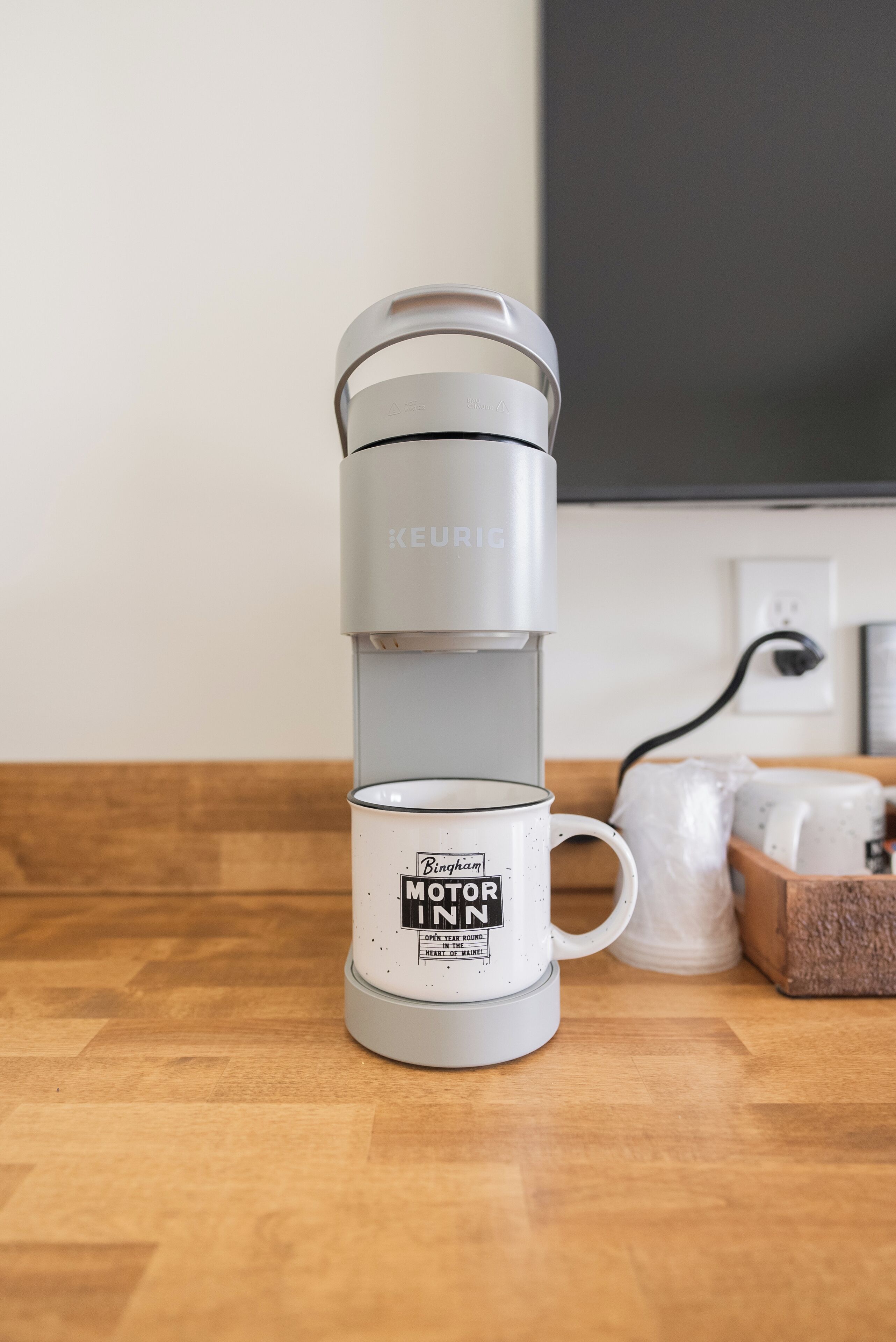 A Keurig coffee maker with a Binham Motor IN mug on a wooden table.