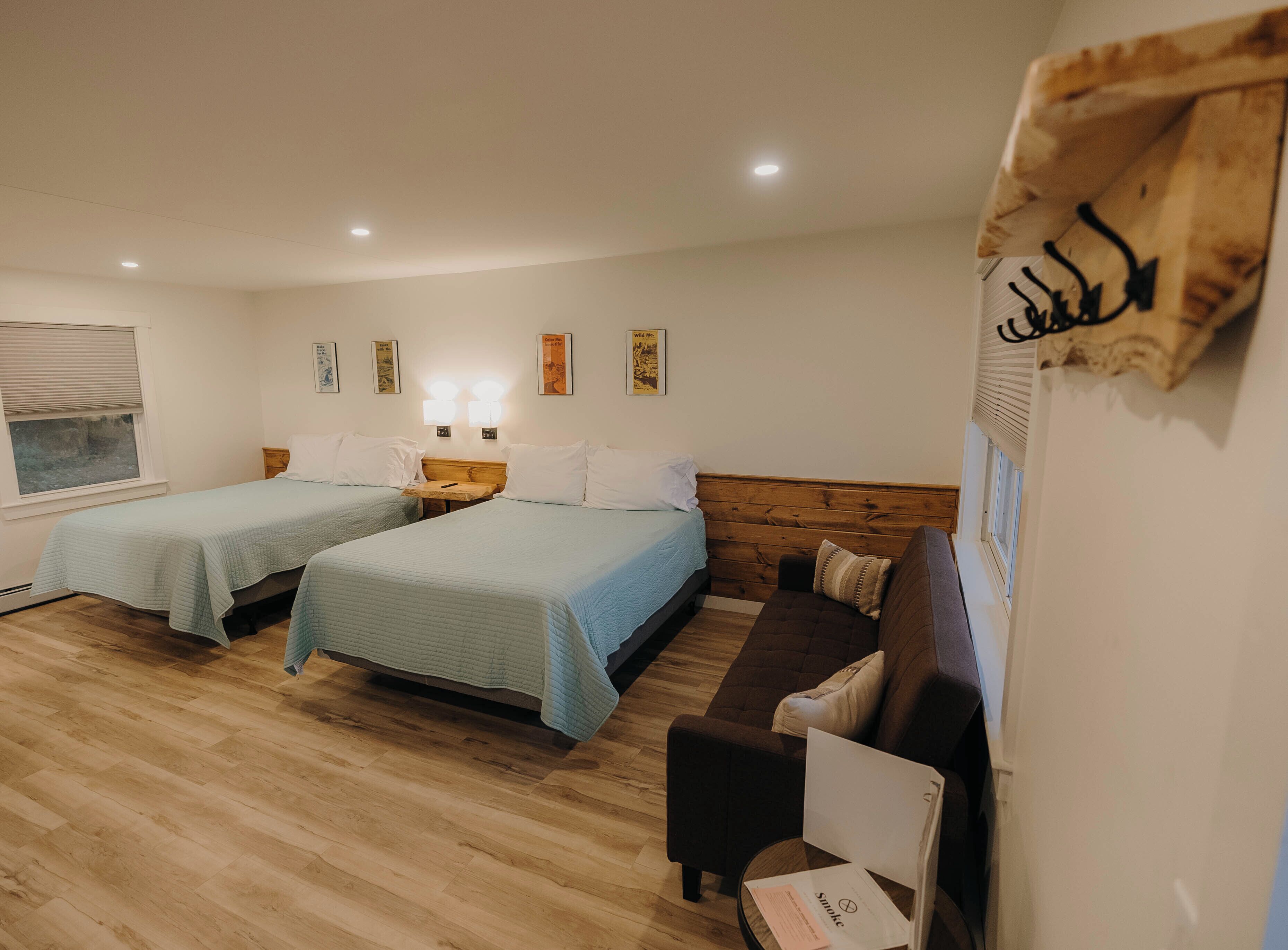 A hotel room with two beds, a wooden floor, a brown sofa, and a small table.