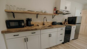 A kitchen with a wooden countertop, white cabinets, a microwave, a coffee maker, a sink, and a stove. - Bingham Motor Inn (Bingham)