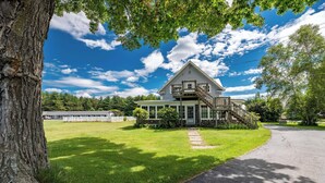 A large, two-story house with a prominent front porch and a wooden staircase leading to a balcony. - Bingham Motor Inn (Bingham)