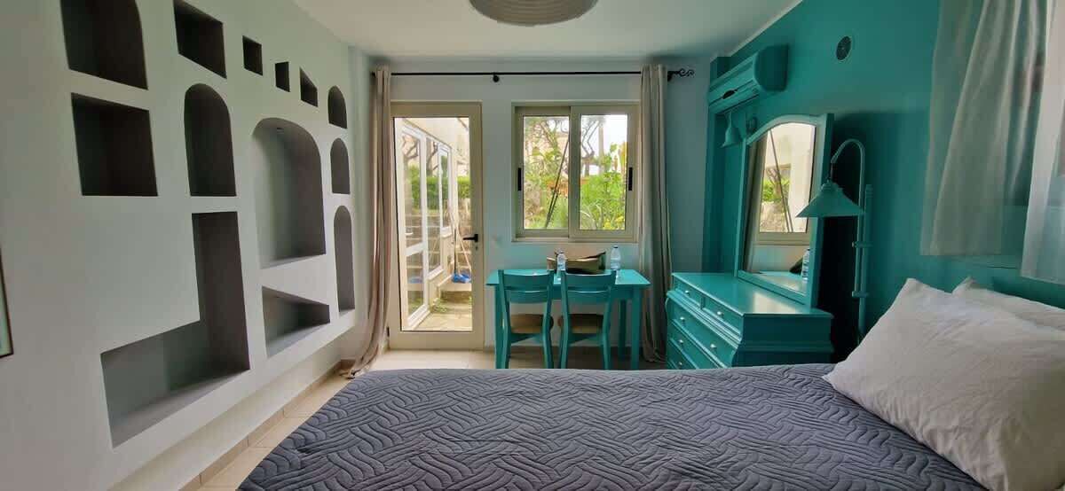 Un dormitorio con cama, escritorio y cómoda. Hay una puerta corrediza de vidrio que da a un espacio exterior.