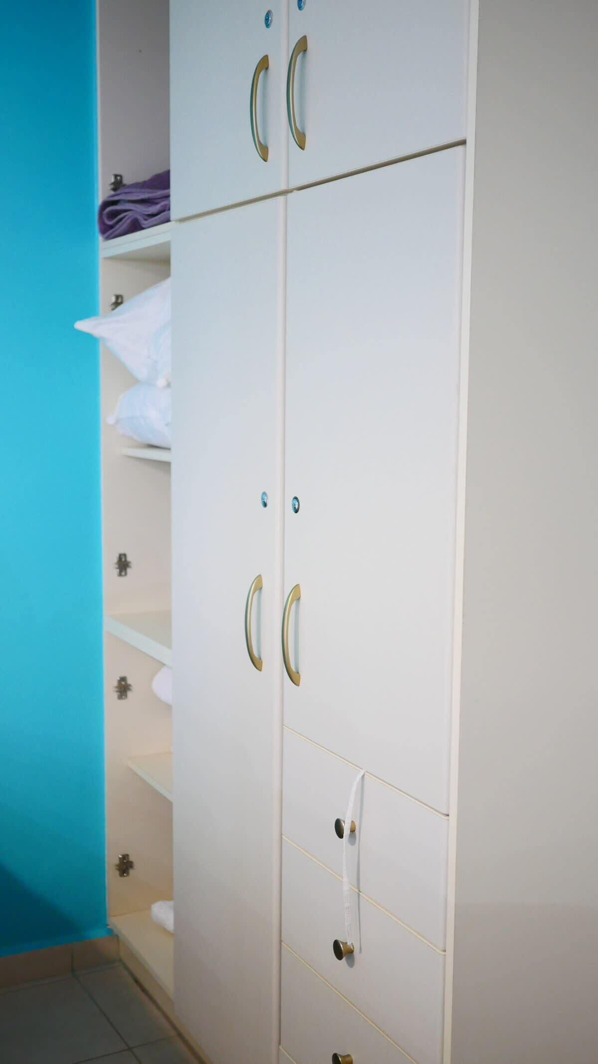 Un armario blanco con dos puertas y varios cajones, con tiradores de latón y una pequeña toalla colgada en una de las puertas.