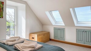A bedroom with a sloped ceiling, skylights, a bed with a green quilted bedspread, a wooden chest of drawers, and light green cabinets. - 1 bedroom accommodation in Drummore, near Stranraer (Drummore, near Stranraer)