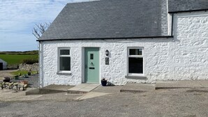 A white building with a green door, a small porch, and a gravel driveway. - 1 bedroom accommodation in Drummore, near Stranraer (Drummore, near Stranraer)