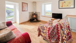 A cozy living room with a fireplace, a sofa, a television, and a view of the outdoors. - 1 bedroom accommodation in Drummore, near Stranraer (Drummore, near Stranraer)