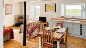 A cozy room with a fireplace, a dining table set for two, and a large window with a view of the outdoors. - 1 bedroom accommodation in Drummore, near Stranraer (Drummore, near Stranraer)