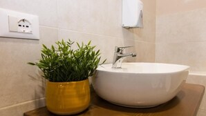Egy fürdőszoba, melyben fehér mosdókagyló, egy sárga növény virágtartóban és egy fehér konnektor található a falon.