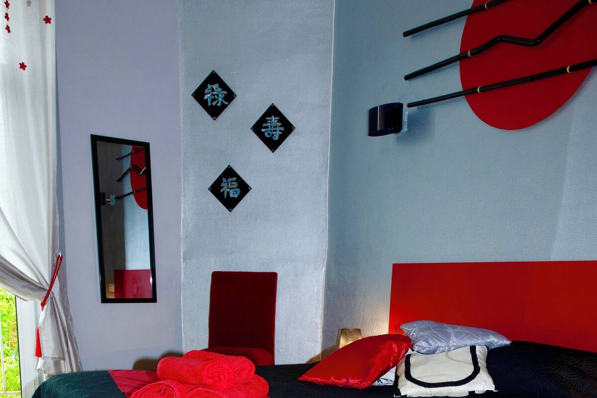Un dormitorio con cama, almohada roja, alfombra roja y pared con detalles decorativos.