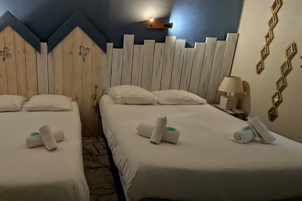 Habitación de hotel con dos camas, cada una con ropa y toallas blancas. La habitación presenta un diseño de cabecero de madera y una pared de acento azul.